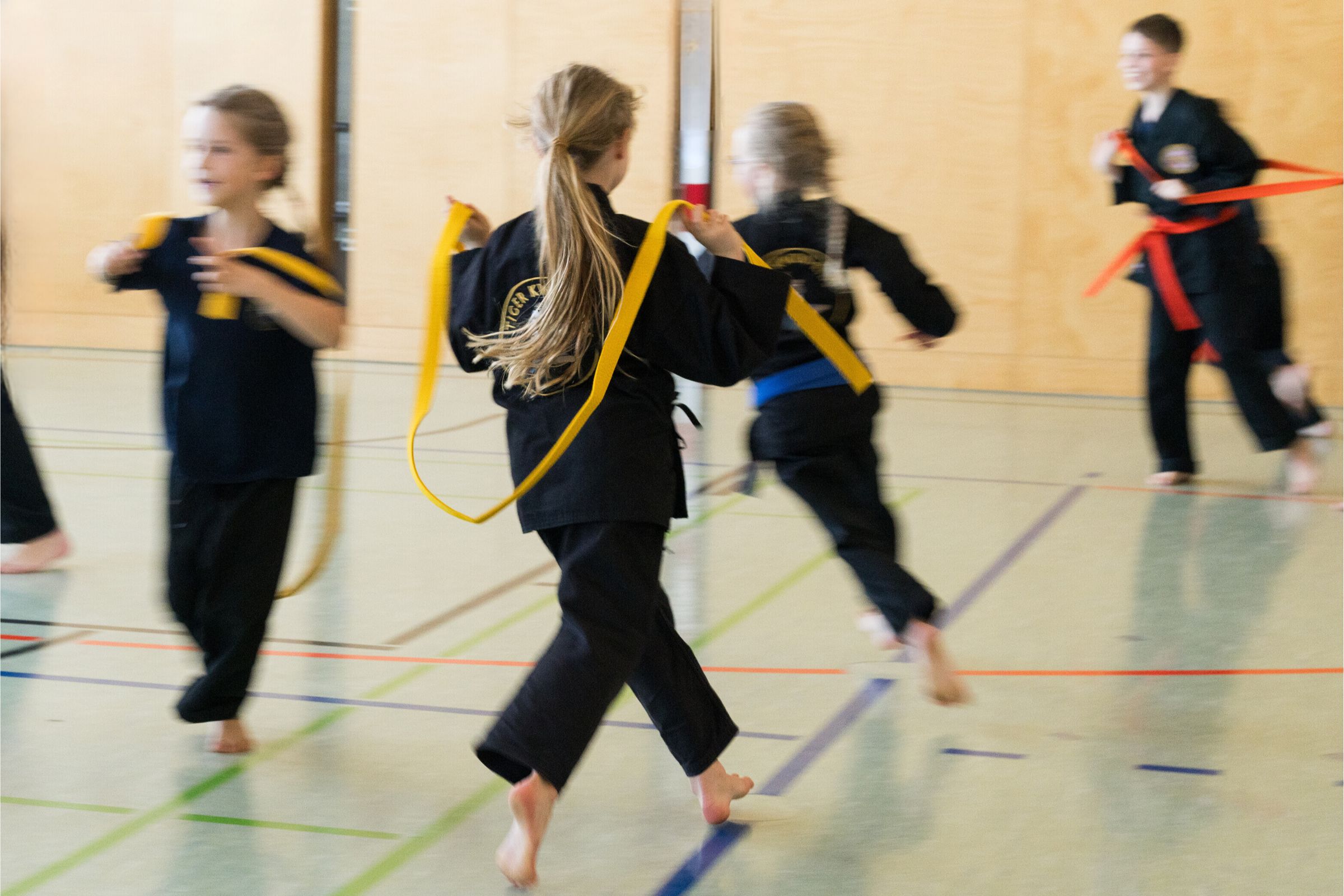 Spielerische Aktivität: Karateschüler spielen fangen in der Turnhalle mit ihren Kampfsportgürteln.