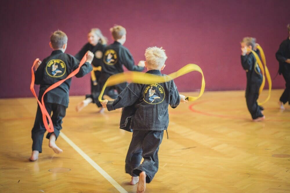 Spielerische Aktivität: Karateschüler spielen fangen in der Turnhalle mit ihren Kampfsportgürteln.