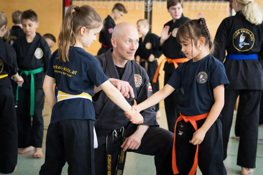 Karatetrainer erklärt zwei Kindern eine Selbstverteidigungstechnik. Körperliche Selbstverteidigung.