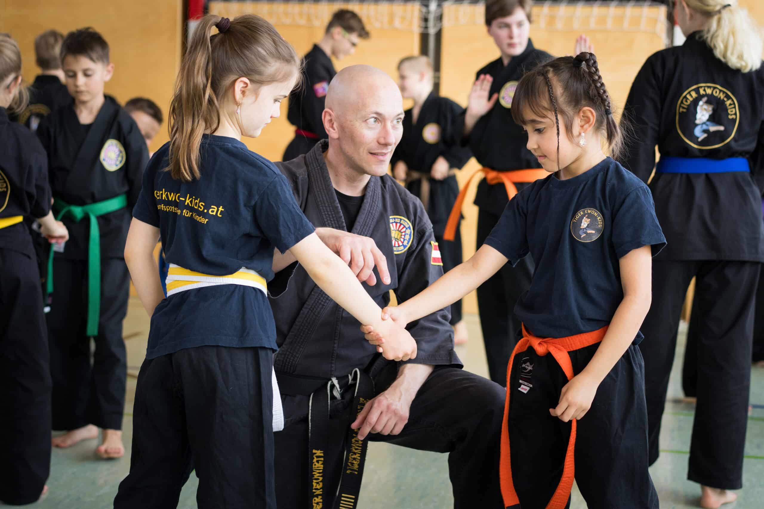 HPL01715 Karatetrainer erklärt zwei Kindern eine Selbstverteidigungstechnik. Körperliche Selbstverteidigung.